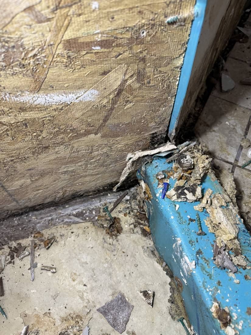 Blue liner at the base of a wall with stained, damaged wood subfloor and debris