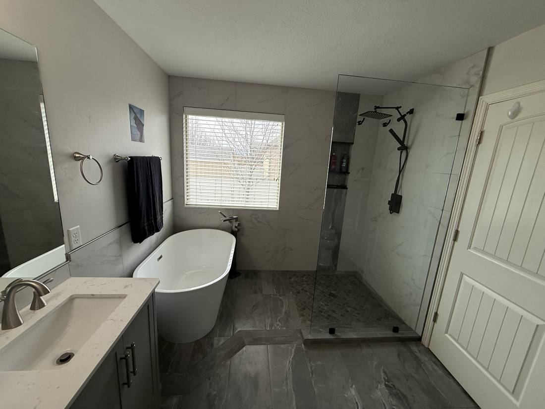 Finished bathroom with a walk-in shower behind a frameless glass panel, a freestanding tub, and a gray stone-look tile floor