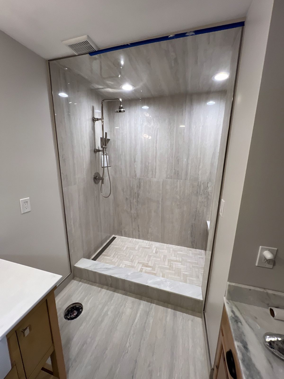 Walk-in shower behind frameless glass, with wood-look wall tile and a linear drain at the back