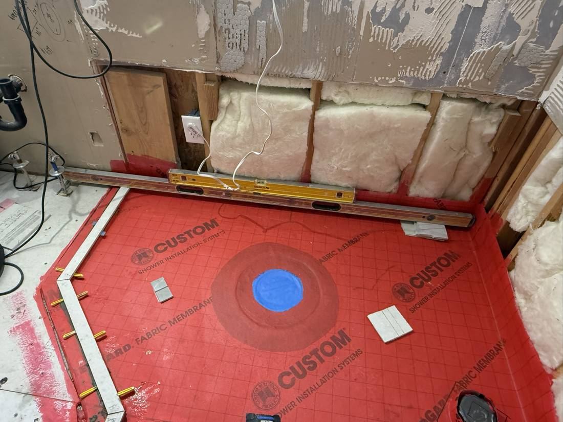 Red waterproofing membrane at the drain and wall base, with a level resting on the wall
