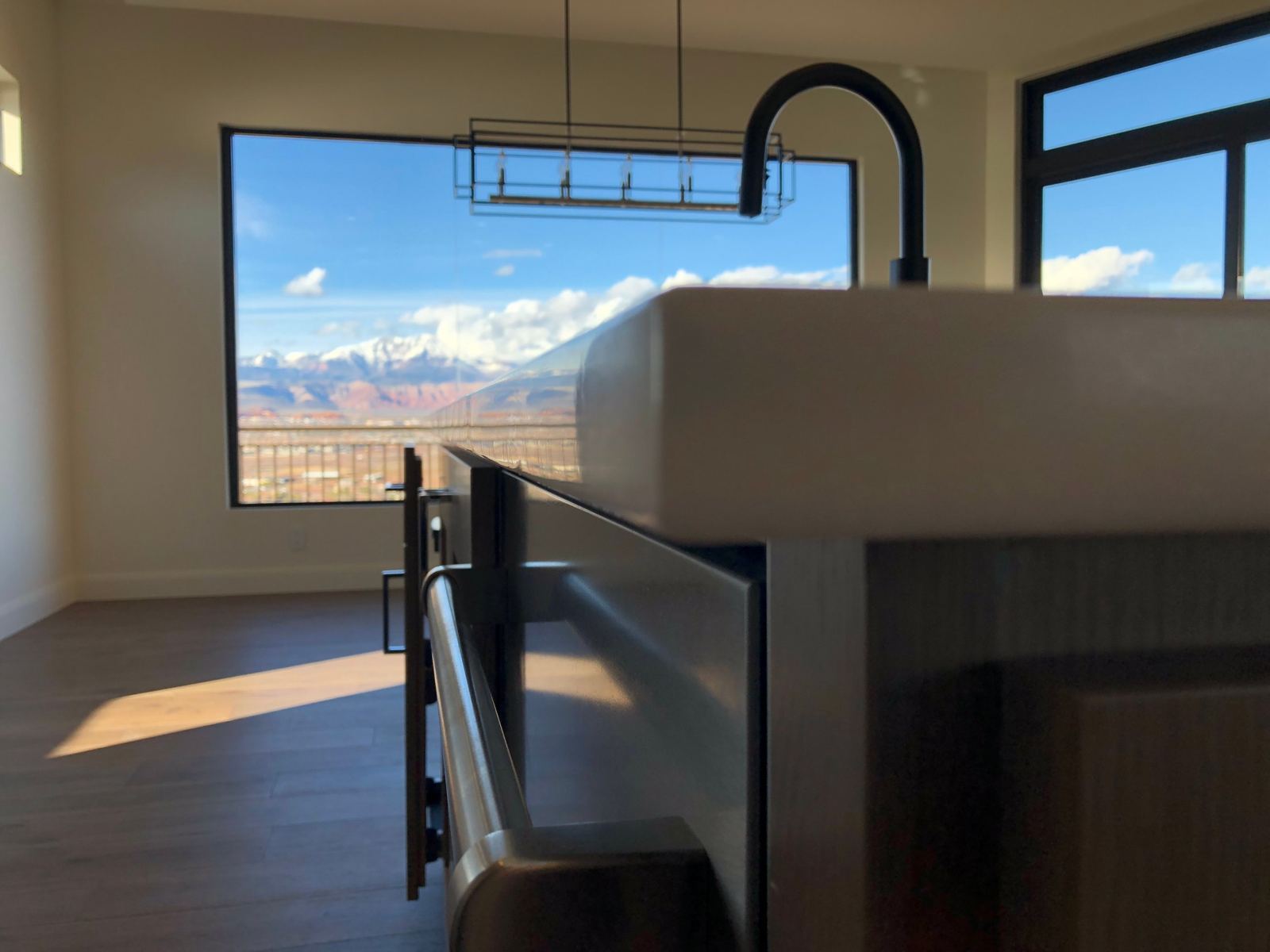 Low view along the smooth, repaired white countertop edge, looking toward a window with red cliffs and snow-capped mountains