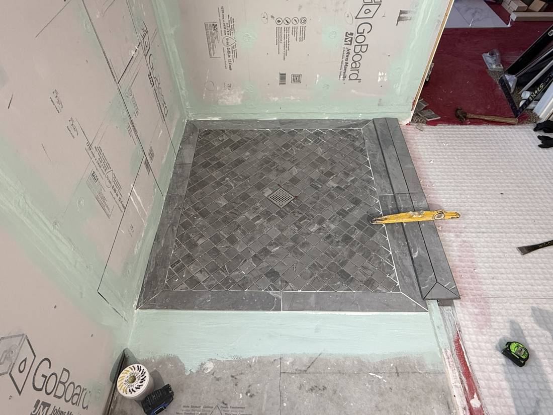 Shower floor tiled with a gray diagonal mosaic and mitered border