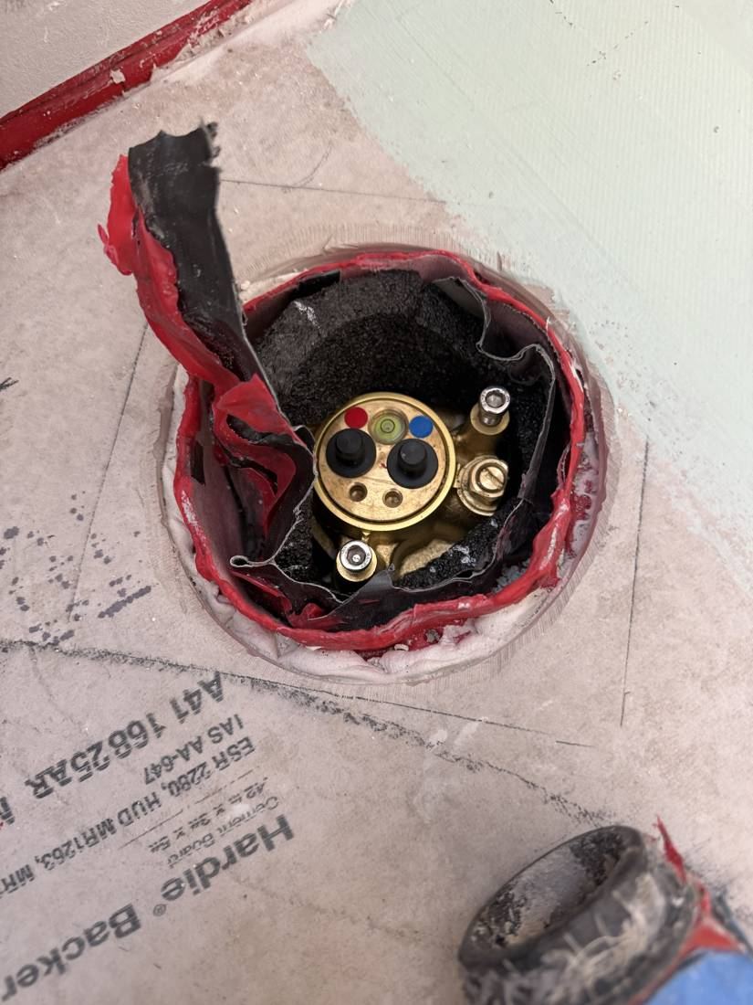 Shower valve body sealed into the wall with red waterproofing and tape